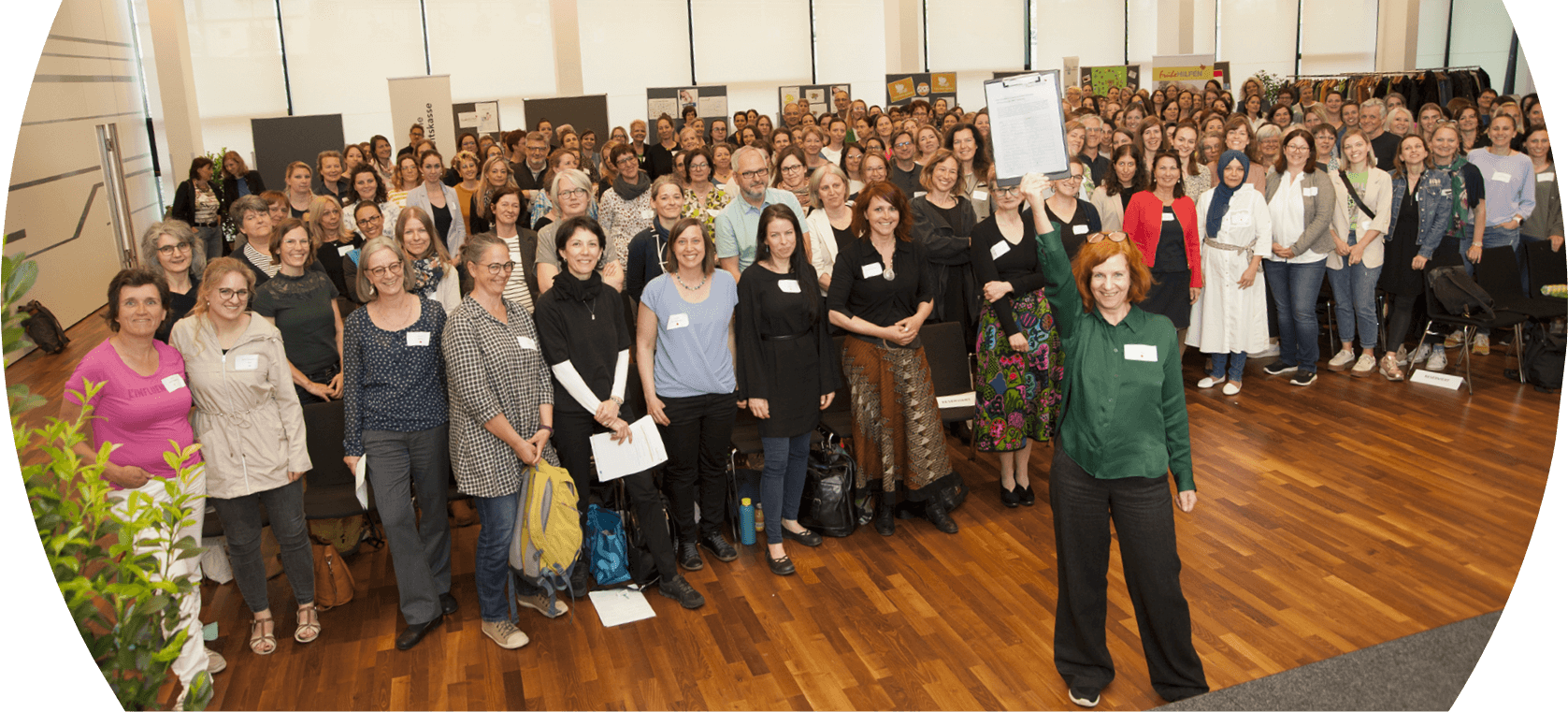 Gruppenfoto von Teilnehmenden der österreichweiten Fachtagung Frühe Hilfen 2023. Zahlreiche Personen versammeln sich im Veranstaltungssaal; im Vordergrund wird die Resolution zur nachhaltigen Finanzierung der Frühen Hilfen symbolisch präsentiert.
