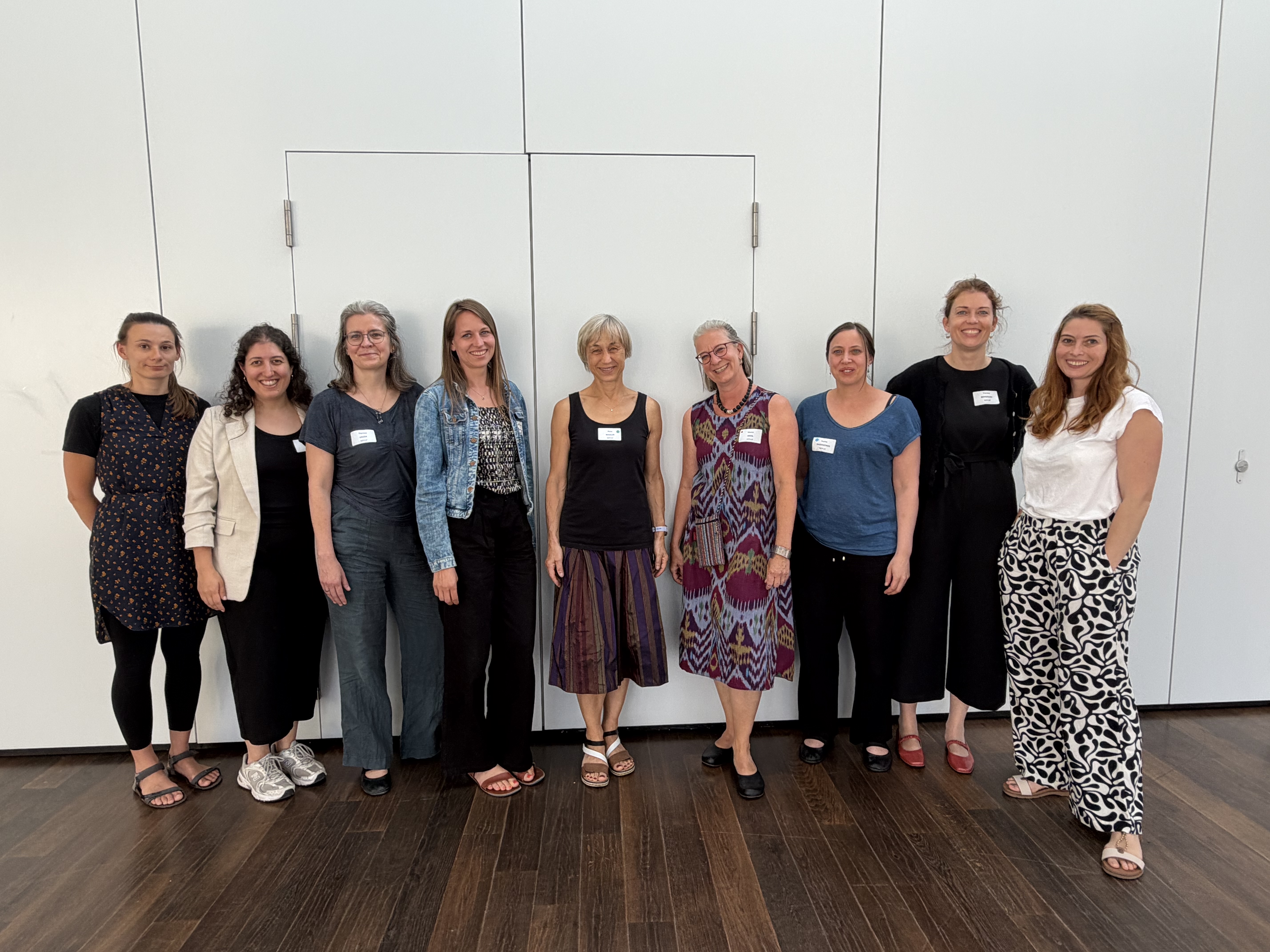 Gruppenfoto des Organisationsteams der Fachtagung Frühe Hilfen 2026. Neun Personen stehen nebeneinander vor einer hellen Wand und blicken in die Kamera.