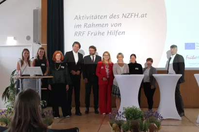 Gruppenfoto von Vortragenden und Projektbeteiligten der Abschlussveranstaltung zum Ausbau der Frühen Hilfen. Die Personen stehen auf der Bühne vor einer Präsentationsfolie zu den Aktivitäten des NZFH.at im Rahmen von „RRF Frühe Hilfen“.