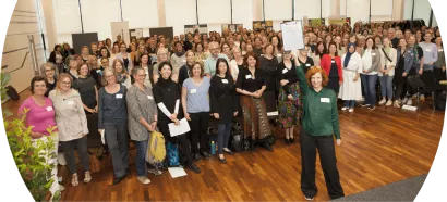 Gruppenfoto von Teilnehmenden der österreichweiten Fachtagung Frühe Hilfen 2023. Zahlreiche Personen versammeln sich im Veranstaltungssaal; im Vordergrund wird die Resolution zur nachhaltigen Finanzierung der Frühen Hilfen symbolisch präsentiert.