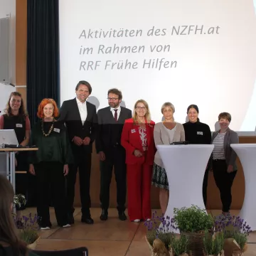 Gruppenfoto von Vortragenden und Projektbeteiligten der Abschlussveranstaltung zum Ausbau der Frühen Hilfen. Die Personen stehen auf der Bühne vor einer Präsentationsfolie zu den Aktivitäten des NZFH.at im Rahmen von „RRF Frühe Hilfen“.