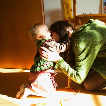 Person und Kleinkind in engem Kontakt in einem Wohnraum. Symbolbild für Frühe Hilfen und familiäre Unterstützung.