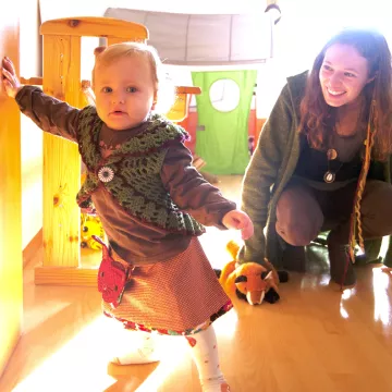 © NZFH.at/Bruckmüller Kleinkind mit begleitender Person im Wohnraum. Symbolbild für Frühe Hilfen Fortbildung und Termine.